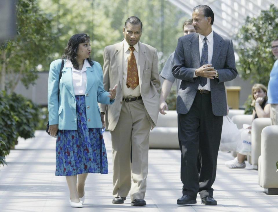 a woman and two men walk inside a sunlight atrium, they wear formal clothes and talk to other another