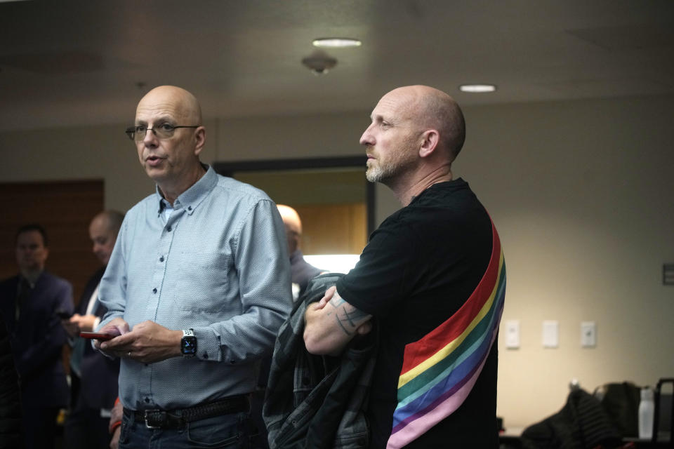 Matthew Haynes and Nic Grzecka, who is wearing a black T-shirt with rainbow stripes across the back in a room with overhead spotlights.