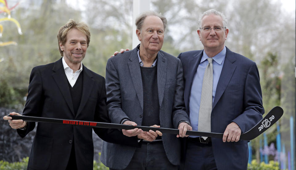 FILE - In this April 11, 2018, file photo, part-owners Jerry Bruckheimer, from left, and David Bonderman pose with Tod Leiweke and a hockey stick during a news conference naming Leiweke as the president and CEO for a prospective NHL expansion team, in Seattle. The NHL Board of Governors is meeting to give final approval to Seattle's bid to add the league's 32nd team. Play would be expected to begin in the 2021-22 season. (AP Photo/Elaine Thompson, File)