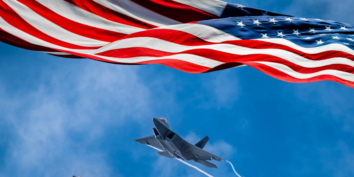 American flag blowing in wind and Lockheed Martin F-22 Raptors flying against sky