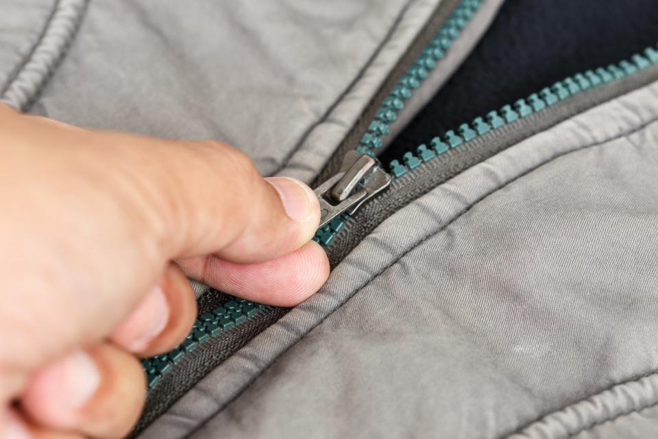 Person pulling the zipper on a grey jacket or bag.