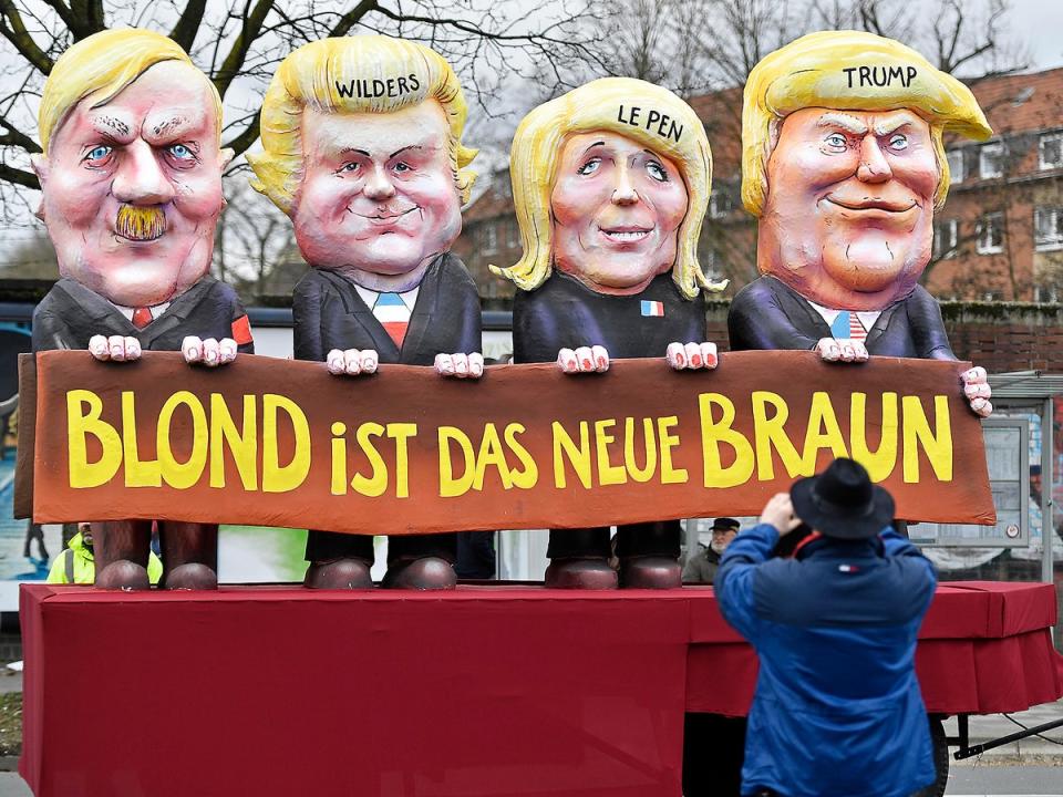 A reveller takes a picture of a carnival float depicting US president Donald Trump with Marine Le Pen, Geert Wilders and Adolf Hitler, reading 'blonde is the new brown' (AP)