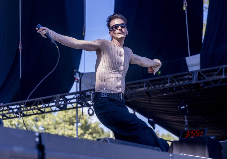 A male singer in a mesh shirt performs onstage