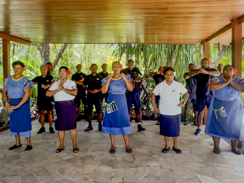 Several staff members of Wakaya Island Resort and Spa wearing blue dresses and white shirts with black skirts on a stone floor