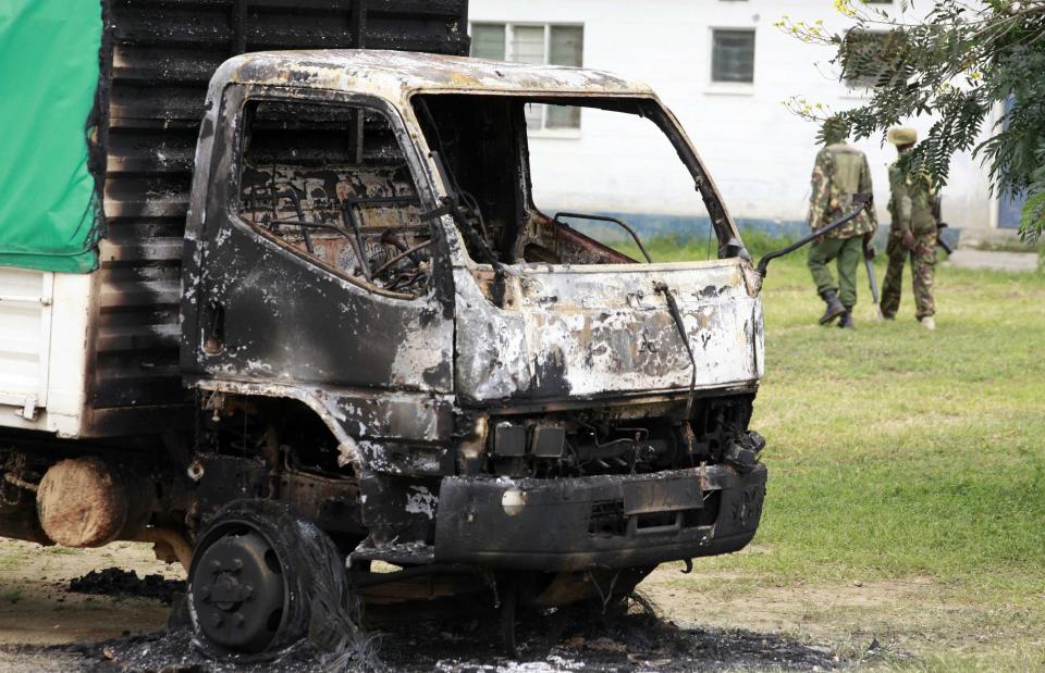 Armed police walk past a truck set on fire by attackers who raided Gamba police station at the Kenyan coast