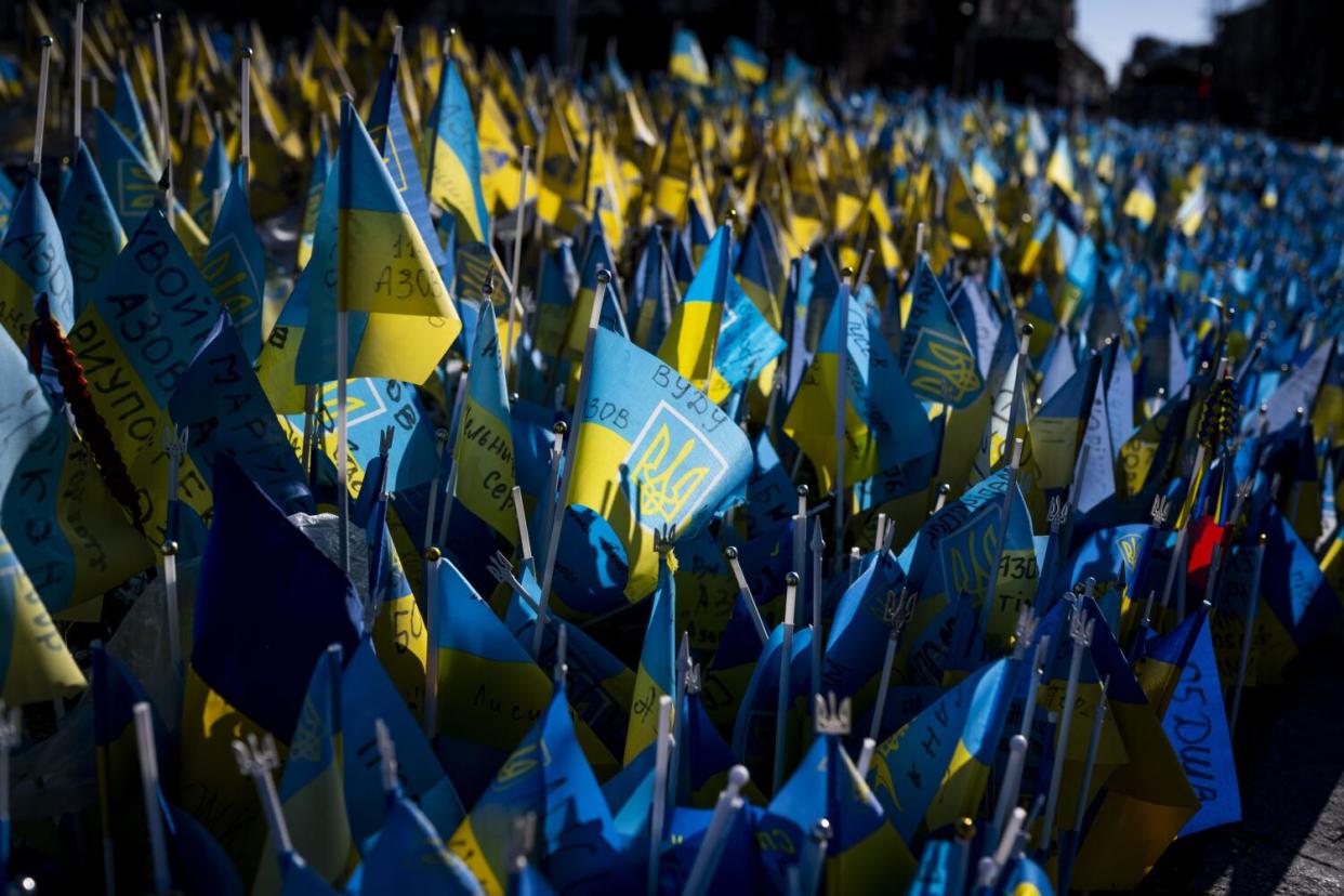 Ukrainian flags with names and dates written on them are crowded together in a sea of yellow and blue.