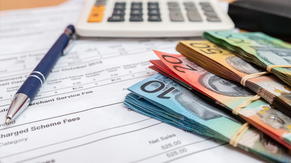 A pen lies on top of paperwork near a calculator and piles of Australian currency.