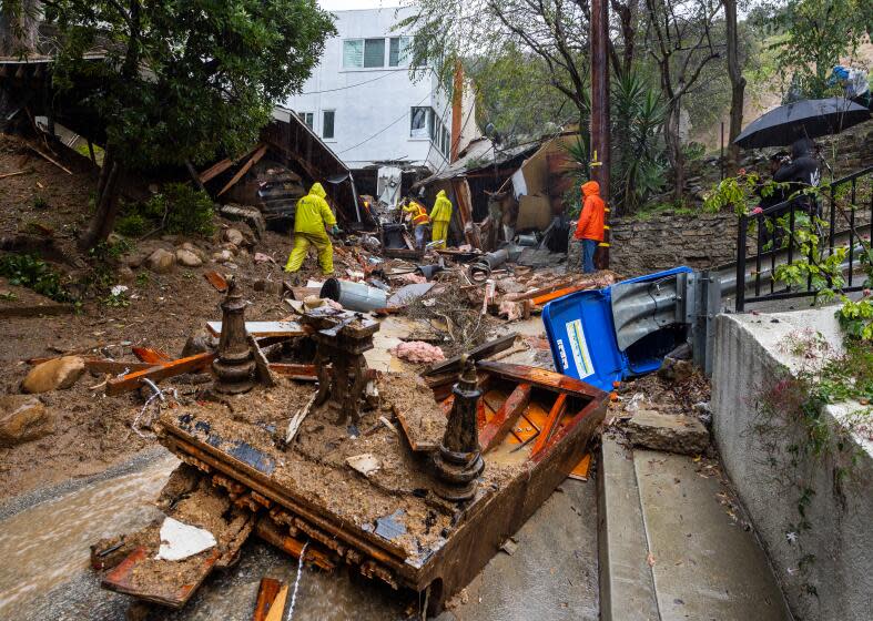 Los Angeles, CA - February 05: A grand piano lies upside down in the middle of Caribou Lane while So Cal Gas workers investigate a Beverly Crest home that was pushed off it's foundation by a mudslide early Monday morning near Beverly Glen Boulevard. No one was home when the mudslide occurred. Caribou Lane Resident Travis Longcore said he and neighbors evacuated themselves after hearing a loud rumbling sound around 2 a.m. The debris completely covers Caribou Lane and caused extensive damage to several others. Rocks, plywood, debris and the piano were washed out of the home. An atmospheric river unleashed heavy rain in Southern California Monday, Feb. 5, 2024. (Allen J. Schaben / Los Angeles Times)