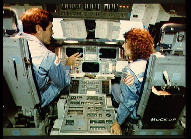 Astronaut Francis R. (Dick) Scobee, STS 51-L commander, briefs Payload specialist Sharon Christa McAuliffe about some of the flight systems of the Space Shuttle during a training session in JSC's Shuttle mission simulator. They are on the flight deck with McAuliffe seated at the pilot's station and Scobee at the commander's station. (NASA)