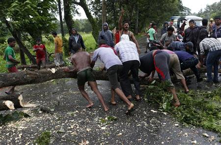 Men try to remove fallen trees from a road due to the rain and wind in Odisha October 12, 2013. REUTERS/Ahmad Masood