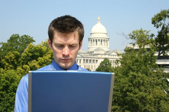 A person on a laptop with the U.S. Capitol building in the background.