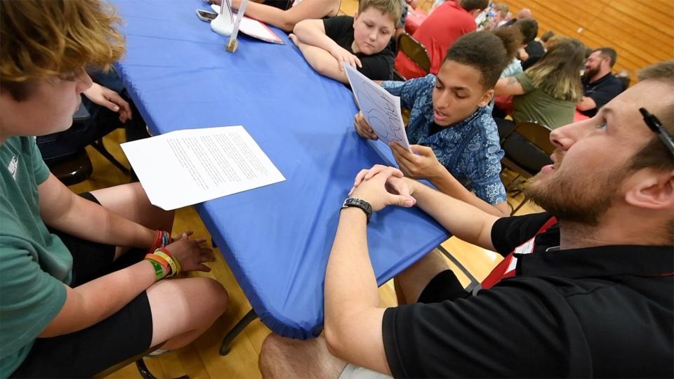 Boden Greener, left, and Josh Alexander, right, both chose their Dover middle-school football coach Justin Rowland as their hero. He listens to their essays during the heroes program at Dover Middle School on May 22, 2024.