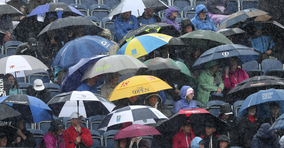 Spectators take cover under umbrellas a heavy rain falls as they watch golfers during the first round of the British Open Golf Championships at Royal Portrush in Northern Ireland, Thursday, July 18, 2019.(AP Photo/Jon Super)