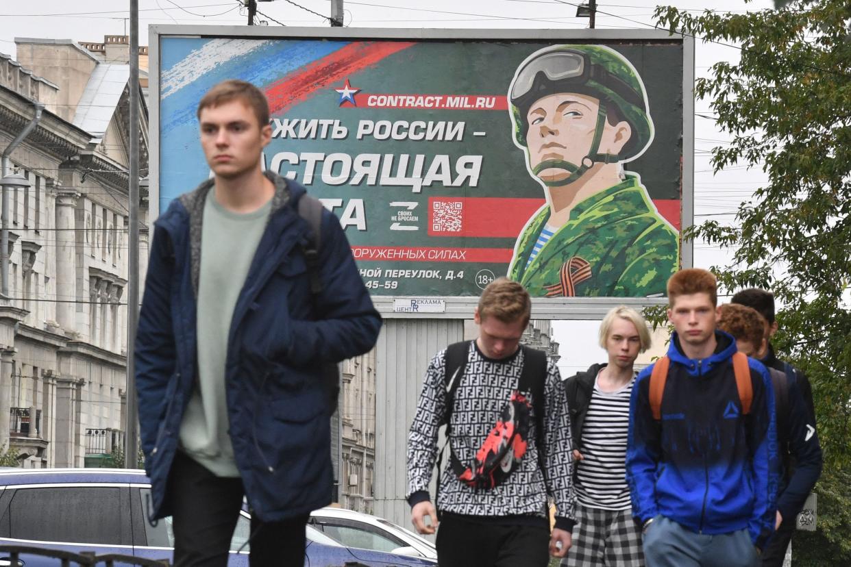 Young men walk in front of a billboard promoting contract army service with an image of a serviceman and the slogan reading "Serving Russia is a real job" in Saint Petersburg on September 29, 2022.