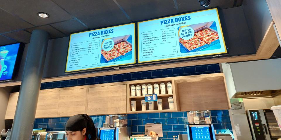 Digital signs at a Greggs cafe in London showing pizza boxes for sale