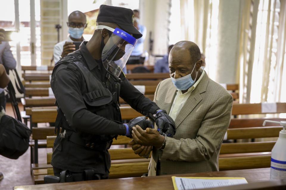 A policeman handcuffs Paul Rusesabagina, right, whose story inspired the film "Hotel Rwanda", before leading him out of the Kicukiro Primary Court in the capital Kigali, Rwanda Monday, Sept. 14, 2020. A Rwandan court on Monday charged Paul Rusesabagina with terrorism, complicity in murder, and forming an armed rebel group, while Rusesabagina declined to respond to all 13 charges, saying some did not qualify as criminal offenses and saying that he denied the accusations when he was questioned by Rwandan investigators. (AP Photo/Muhizi Olivier)