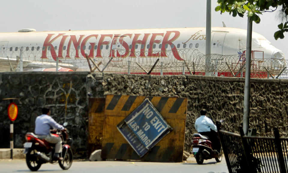 Commuters drive past a stationary aircraft belonging to Kingfisher airlines at the domestic airport in Mumbai, India, Tuesday, March 20, 2012. The severely cash-strapped airlines may now face the risk of cancellation of its flying permit after the Directorate General of Civil Aviation (DGCA) expressed doubts on its ability to maintain a steady schedule with a declining number of operable aircrafts and ongoing problems with pilots leaving the company.(AP Photo/Rafiq Maqbool)