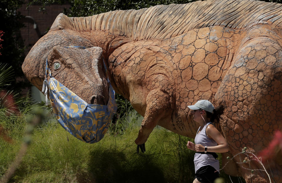 A jogger runs past a mask clad Acrocanthosaurus at the Witte Museum in San Antonio, Thursday, May 28, 2020. The museum has been closed due to the COVID-19 pandemic and is scheduled to reopen May 30th. (AP Photo/Eric Gay)