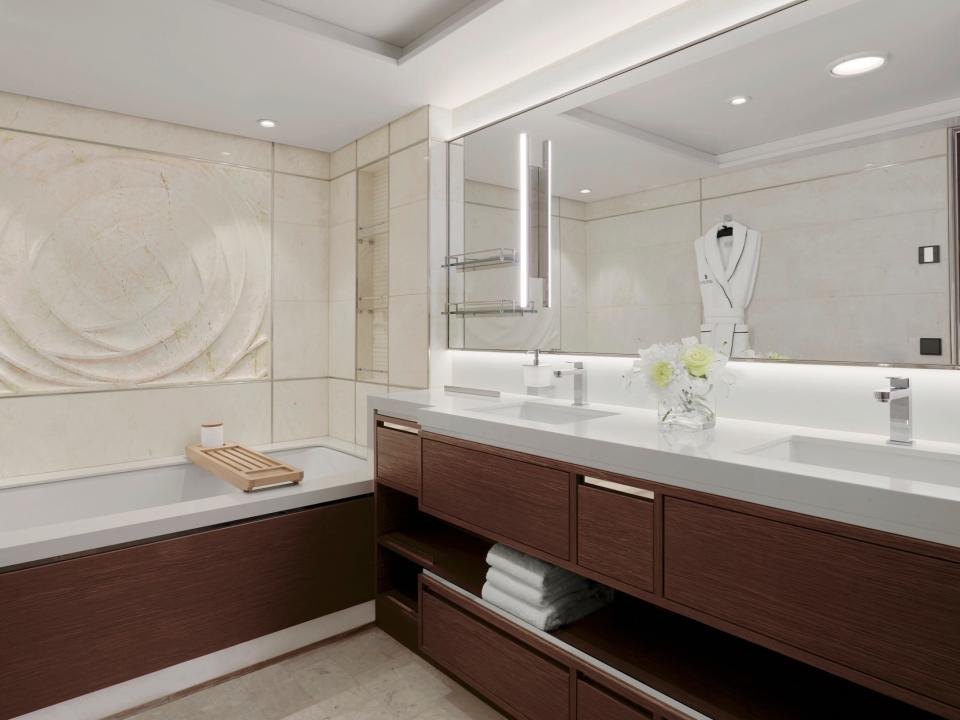 A bathroom with a bathtub, double vanity, robe hanging on the wall.