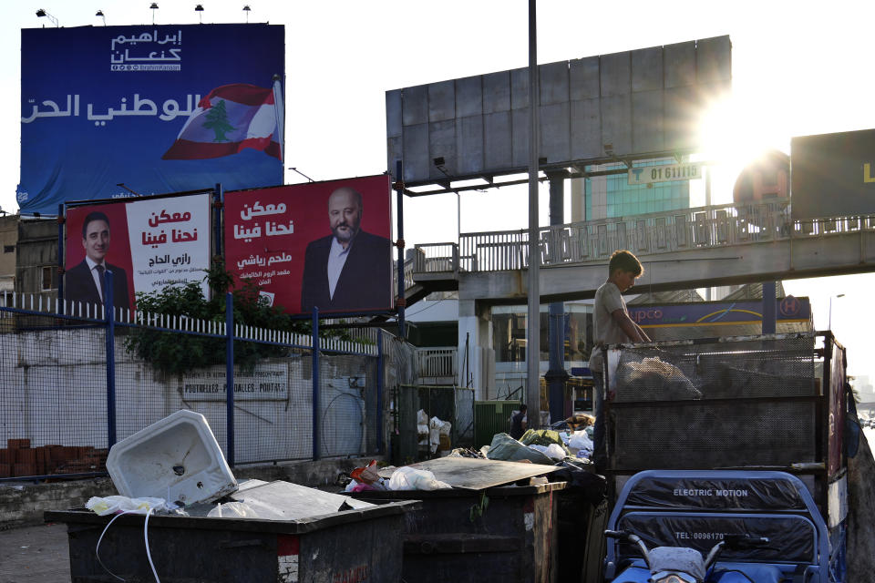 A boy looks in the trash for recyclable items to resell in front of campaign posters for candidates in the upcoming parliamentary elections in Beirut, Lebanon, Monday, May 9, 2022. Given Lebanon's devastating economic meltdown, Sunday's parliament election is seen as an opportunity to punish the current crop of politicians that have driven the country to the ground. Yet a sense of widespread apathy and cynicism prevails, with many saying it is futile to expect change. The Arabic text on the banners read "Melhem Riachi, Razi al-Haj, With you we can, bottom, Ibrahim Kanaan the Free Patriotic Movement (Christian group), above." (AP Photo/Hassan Ammar)