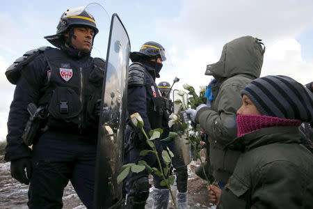 Youngs migrants holding white flowers face French riot police officers who secure the area near makeshift shelters during the partial dismantlement of the camp for migrants called the "Jungle" in Calais, France, March 7, 2016. REUTERS/Pascal Rossignol