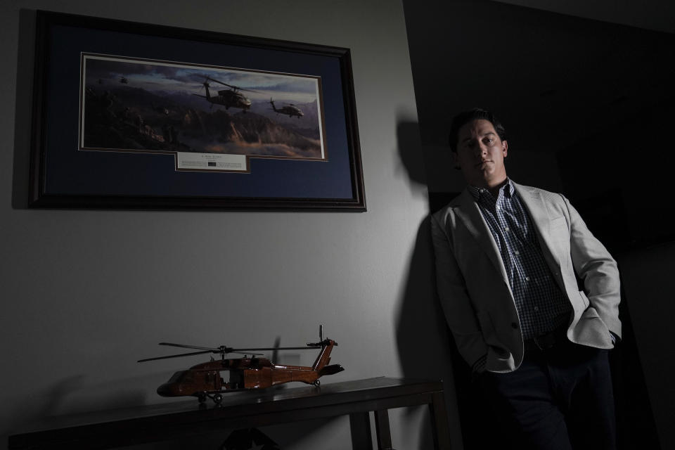 U.S. Army veteran Andrew Brennan, 36, poses for a photo near a display with a UH-60 Black Hawk in his home in Baltimore on Wednesday, June 30, 2021. The former Army captain who flew combat missions in Afghanistan lost one of his closest friends, pilot Bryan Nichols, who was killed along with the entire crew when their Chinook helicopter was shot down in 2011, killing 30 Americans, seven Afghan soldiers and one interpreter. It was the single deadliest day for U.S. troops during the war. (AP Photo/Julio Cortez)