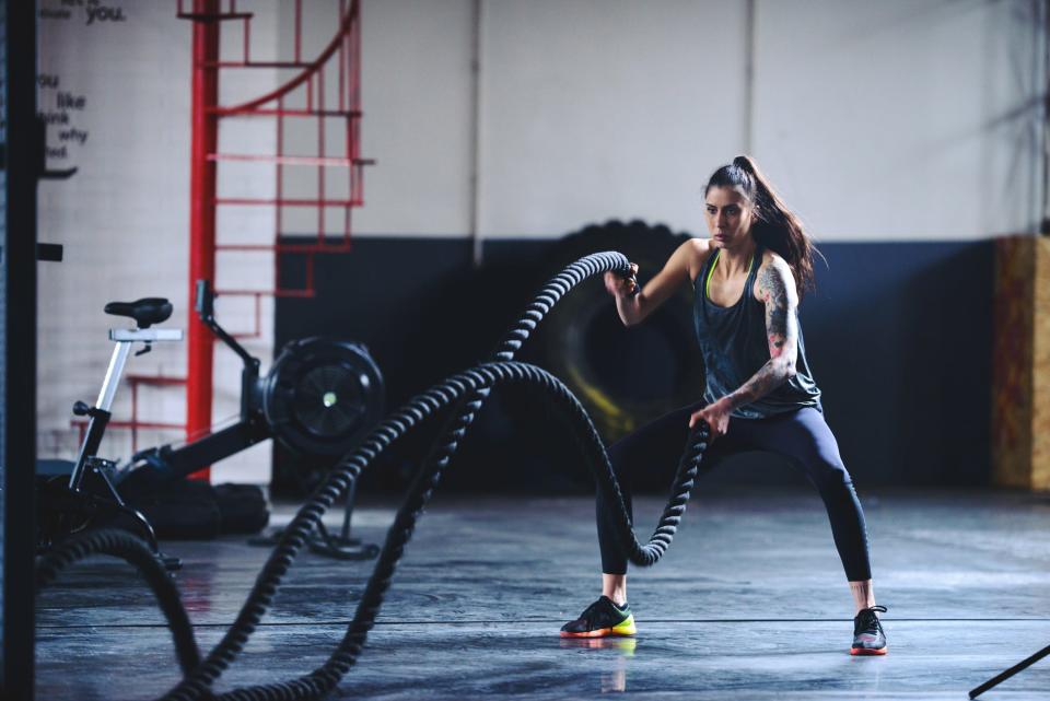 A woman in a gym performing battle rope exercise with alternating waves.