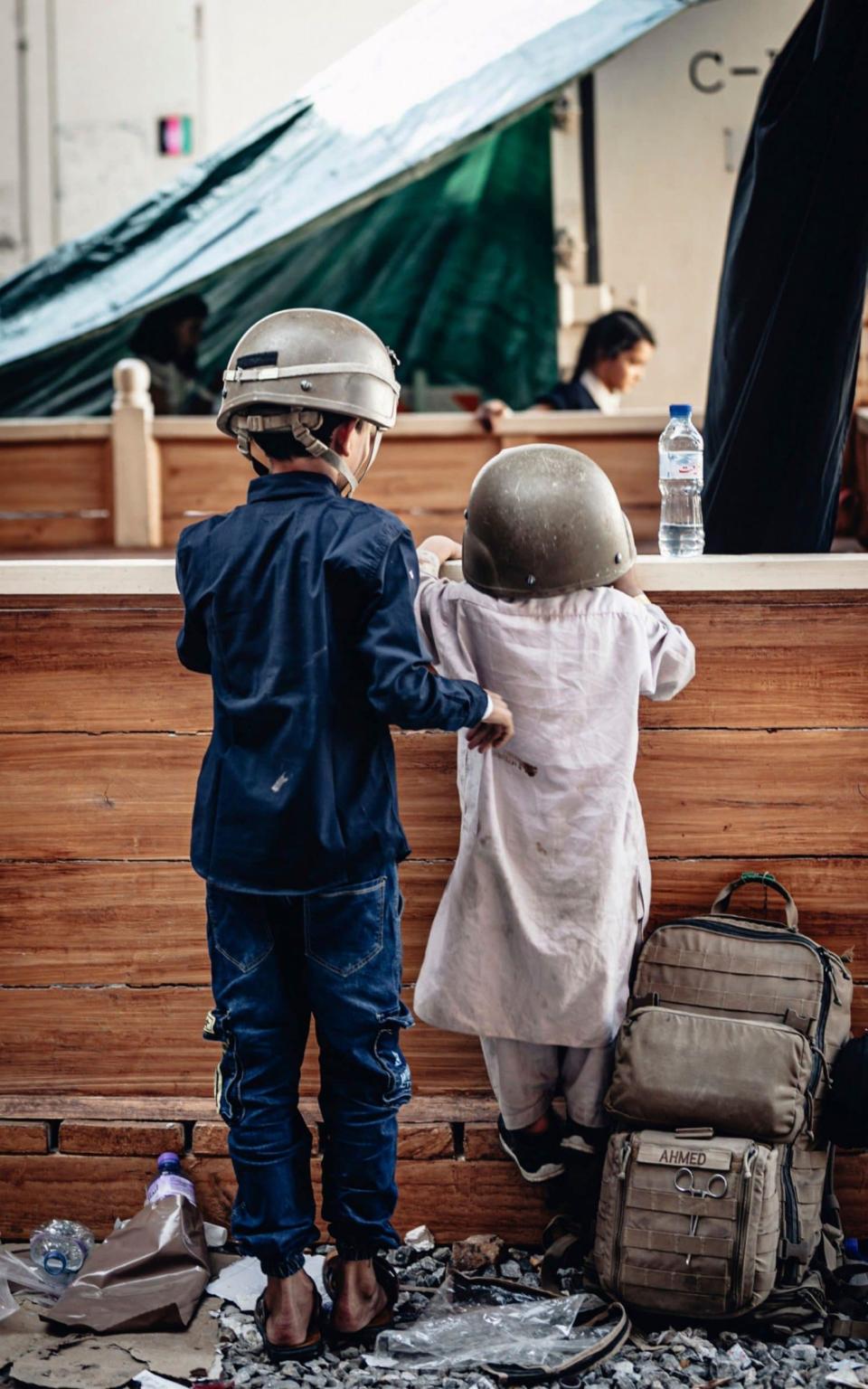 Afghan children play with military helmets while waiting for evacuation from Hamid Karzai International Airport in August - Alamy