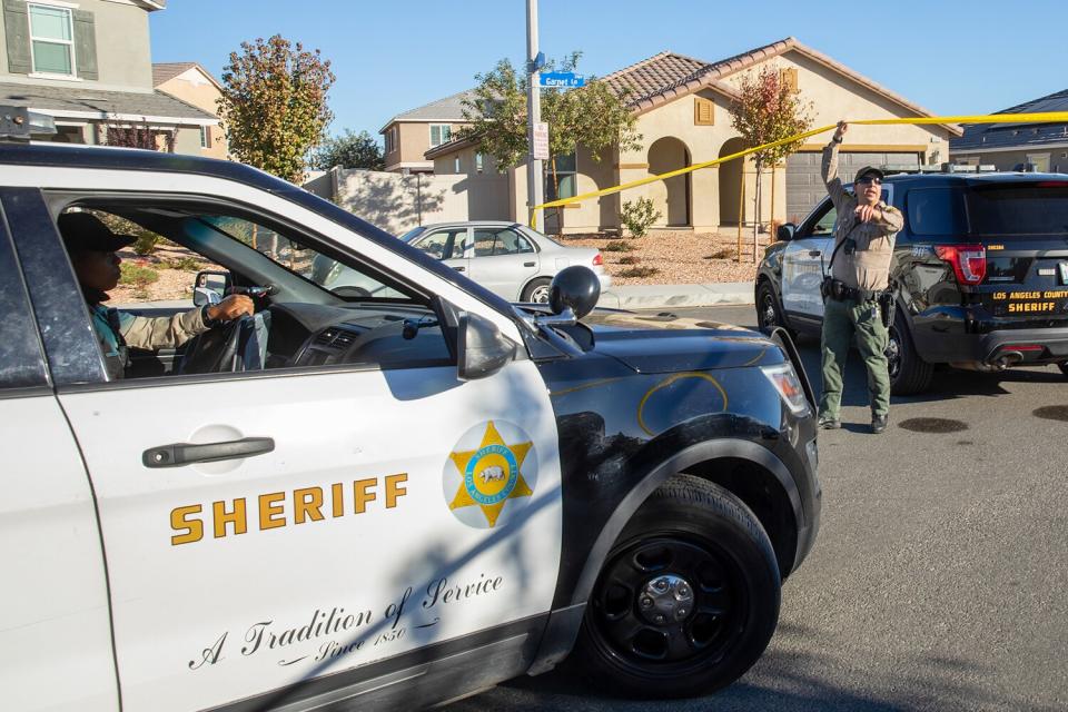 A deputy lifts up crime scene tape next to a sheriff's cruiser