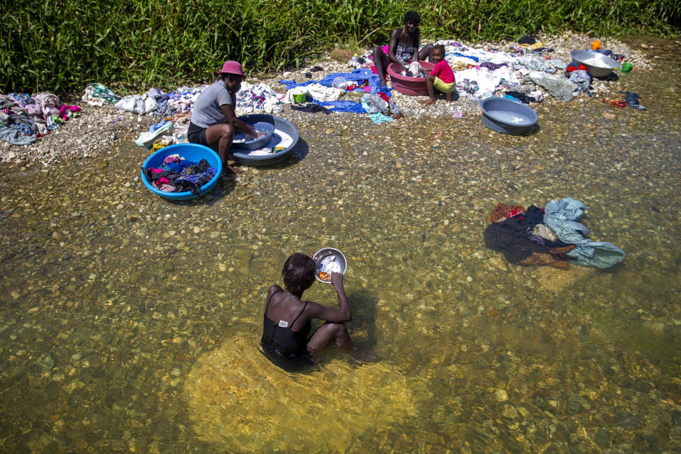 Geraldine Pierre 14, front, eats as she takes a break from washing clothes with her family in the Meille River near a former UN base in Mirebalais, Haiti, Monday, Oct. 19, 2020. Ten years after a cholera epidemic swept through Haiti and killed thousands, families of victims still struggle financially and await compensation from the United Nations as many continue to drink from and bathe in a river that became ground zero for the waterborne disease. (AP Photo/Dieu Nalio Chery)
