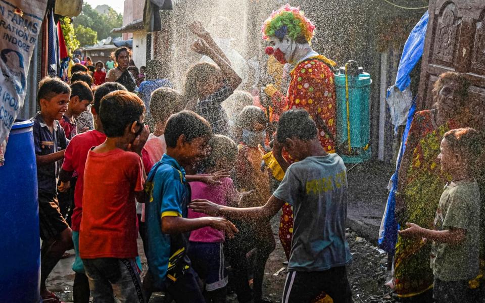 Children play as Ashok Jagannath Kurmi, a 36-year-old social worker, sprays disinfectant liquid while dressed in a clown costume at a slum. Kurmi, 36, who works for a pharmaceutical company to earn money, says that he dresses in different costumes during his outreach to help spread official messages about the Covid-19 coronavirus to both children and adults. - Fariha Farooqui/Getty Images
