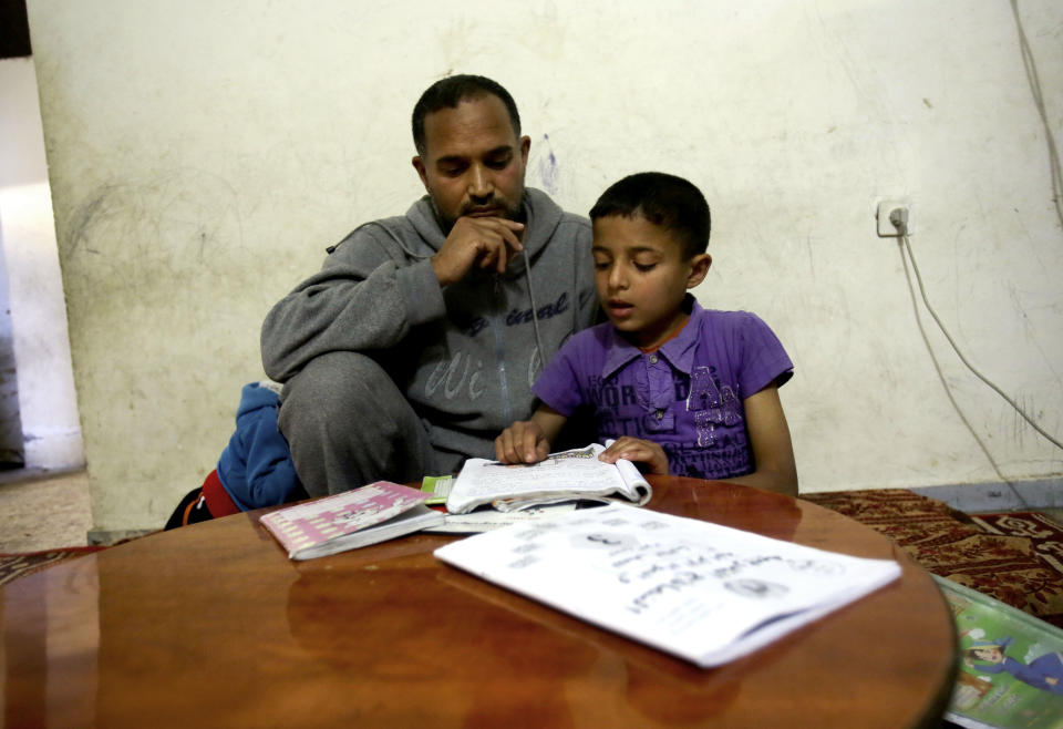 In this Monday, May 12, 2014 photo, Palestinian refugee Hassan Sattari, 40, listens to his son Abdel-Hai, 9, while he helps him prepare for final exams at their home in Khan Younis Refugee Camp, the southern Gaza Strip. Hassan said he doesn’t believe Israel would ever agree to take back large numbers of refugees who, along with their descendants, now number more than 5 million across the Middle East. Instead, he’s banking on education for his children to help them escape. (AP Photo/Adel Hana)