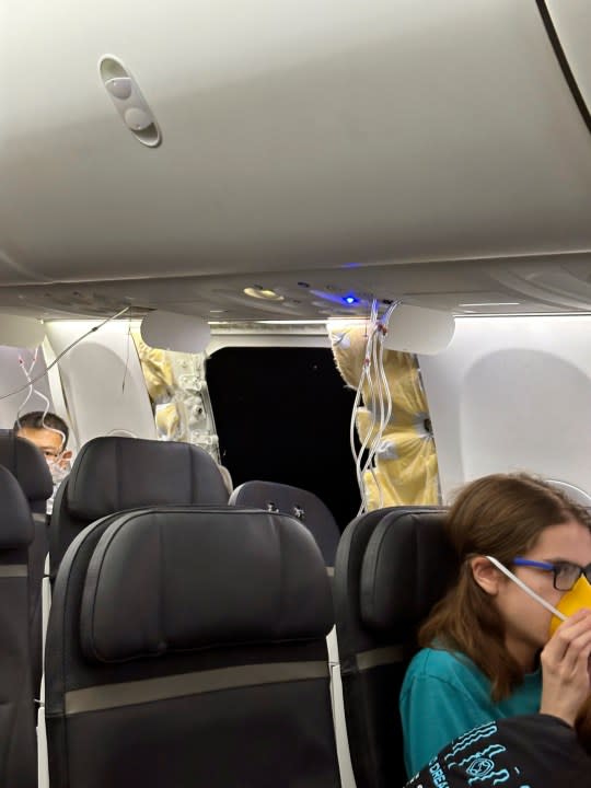 This image provided by Kelly Bartlett shows passengers near a hole in the fuselage of an Alaska Airlines Boeing 737 Max 9, Flight 1282, which was forced to return to Portland International Airport on Friday, Jan. 5, 2024. (Kelly Bartlett via AP)