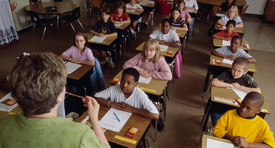 Stock image of students in school listening to a teacher.