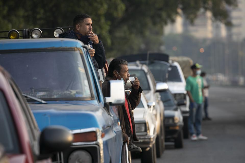 Men stand close to their vehicles as they wait for hours to fill up with gasoline in Caracas, Venezuela, Thursday, April 02, 2020. Lines at gas stations around the country's capital are getting longer and longer with some citizens saying it was only this bad during the oil worker's strike of 2002. (AP Photo/Ariana Cubillos)