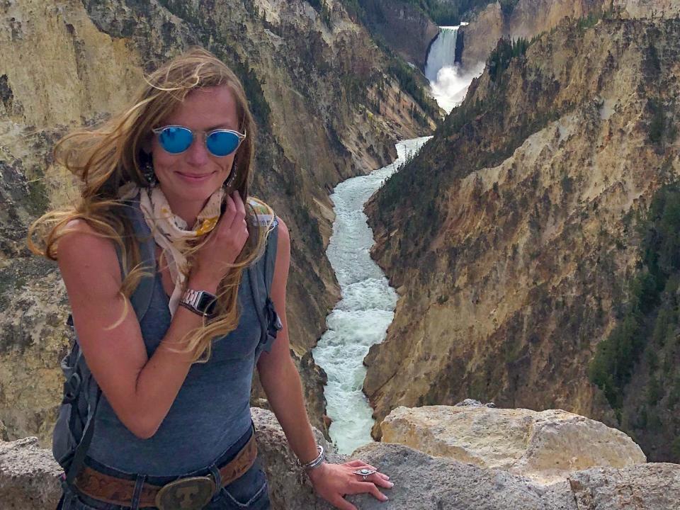 Emily standing in front of a waterfall and its stream at Yellowstone National Park.