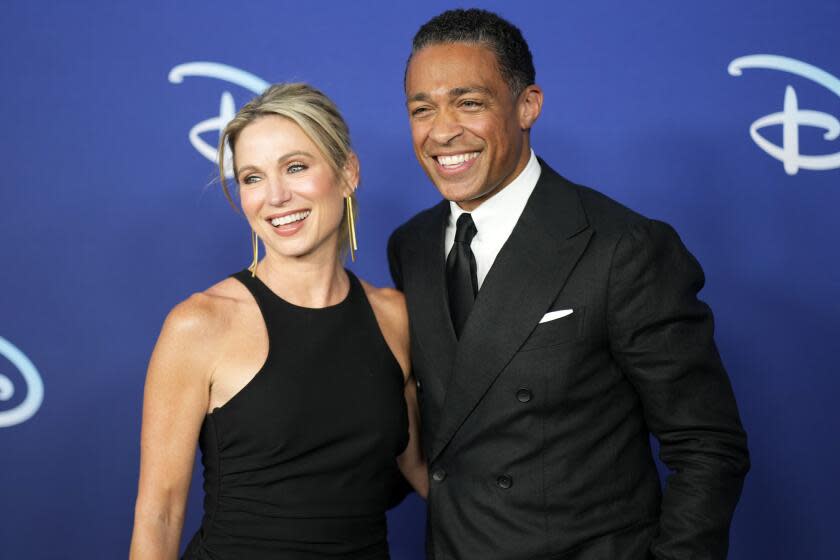 A blond woman in a black dress and a dark-haired man in a black suit smiling and posing for a photo together