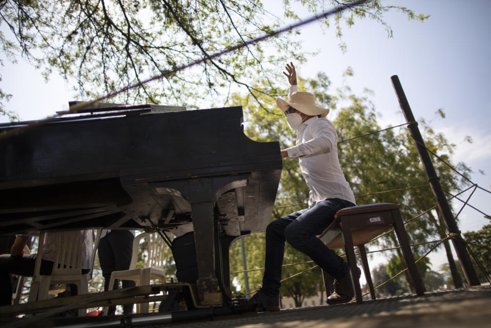 Con mascarillas para frenar la propagación del nuevo coronavirus, el pianista, compositor y director José Agustín Sánchez guía a sus compañeros músicos en la plataforma de un camión de dieciocho ruedas para una gira musical llamada "Desinfección musical", en Barquisimeto, Venezuela, el jueves 4 de marzo. 2021. Sánchez, quien el año pasado comenzó a tocar lo que él llama su "Vacuna Musical" para pacientes con COVID, ahora se une a otros músicos mientras recorren la ciudad tocando sus composiciones originales para cualquiera que quiera escuchar. (AP Foto/Ariana Cubillos)