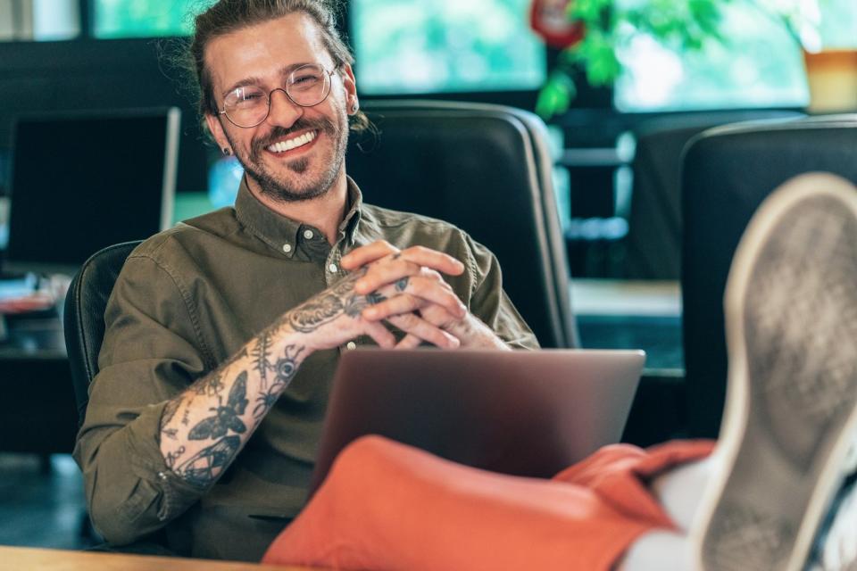 A smiling person with their feet propped up on their desk.