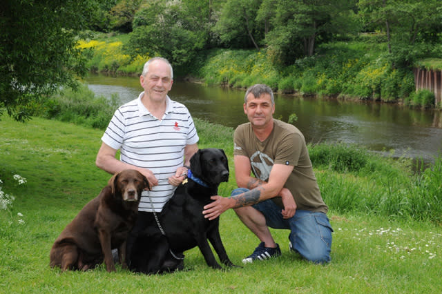 Pete Alderson (L) who was saved by his daughters dog Wispa(brown) and his neighbour Martin Green after falling in the river Wye at Hunderton when out walking dogs the Wispa and George. See News Team story NTIDOG; Pete Alderson, 73, was walking his daughter's chocolate Labrador Wispa and his brother-in-law's black Labrador George when they both went into the water. The dad-of-two started to walk down a track to get closer to call them back but slipped and fell into the River Wye near his home at 9.40am last Friday (27/5). Pete, who can't swim, began to drown after he panicked when he swallowed water with his mouth open. But just as he started to slip into unconsciousness he realised seven-year-old Wispa was paddling near him. Pete managed to grab on to the lifesaving dog who quickly swam towards the shore where he was able to cling on to some reeds and the bank.