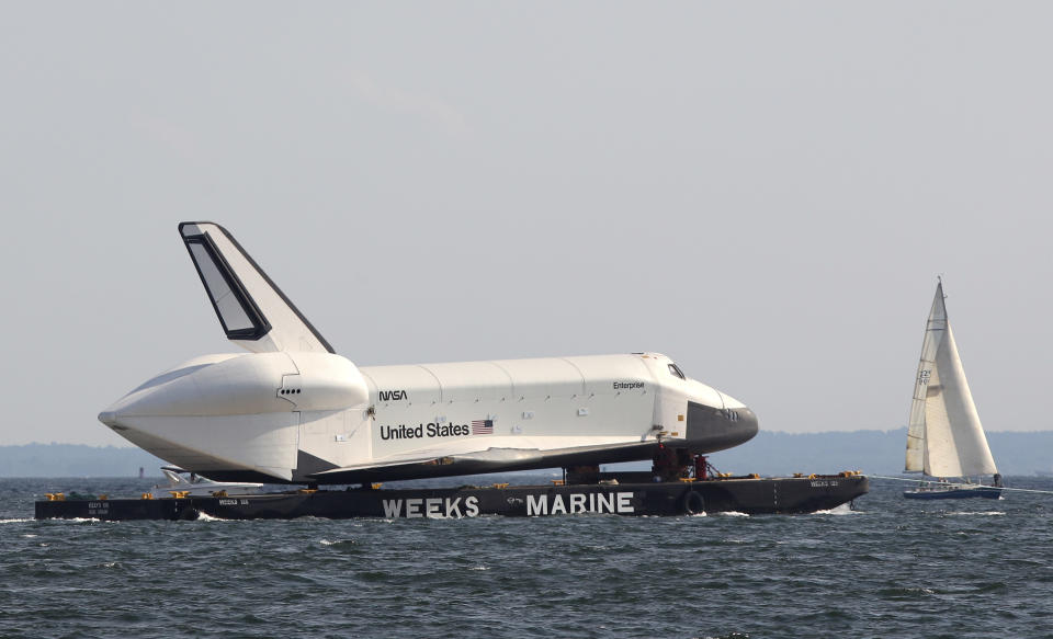 A sailboat passes the space shuttle Enterprise as it is towed past Coney Island in New York, Sunday, June 3, 2012. The prototype space shuttle that arrived in New York City by air earlier this spring is on the move again, this time by sea, to it's final resting place at the Intrepid Sea, Air and Space Museum on the west side of Manhattan. (AP Photo/Seth Wenig)