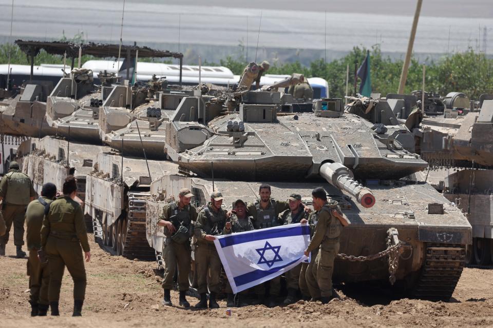 A group of Israeli soldiers holds an Israeli flag as they gather with military vehicles at an undisclosed position (EPA)