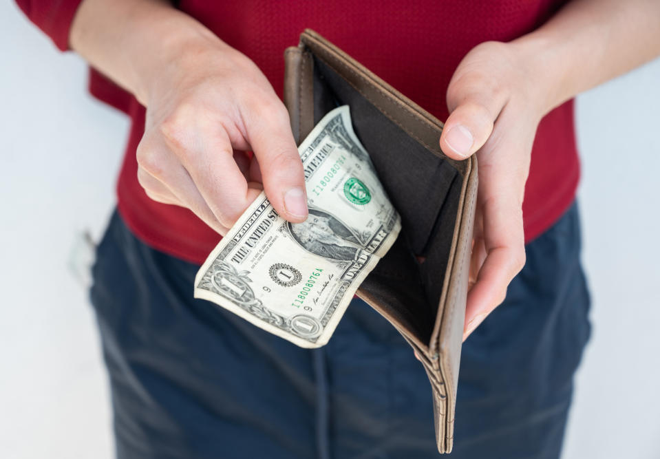 Person holding a wallet with one dollar, indicating insufficient funds or budgeting woes