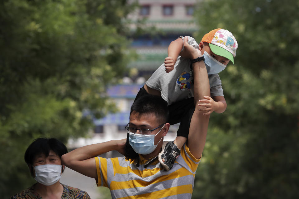 A man wearing a face mask to protect against the new coronavirus puts his masked child on his shoulders as they visit to a shopping district in Beijing, Sunday, July 19, 2020. China on Sunday reported another few dozen of confirmed cases of the coronavirus in the northwestern city of Urumqi, raising the total in the country's most recent local outbreak to at least 30. (AP Photo/Andy Wong)