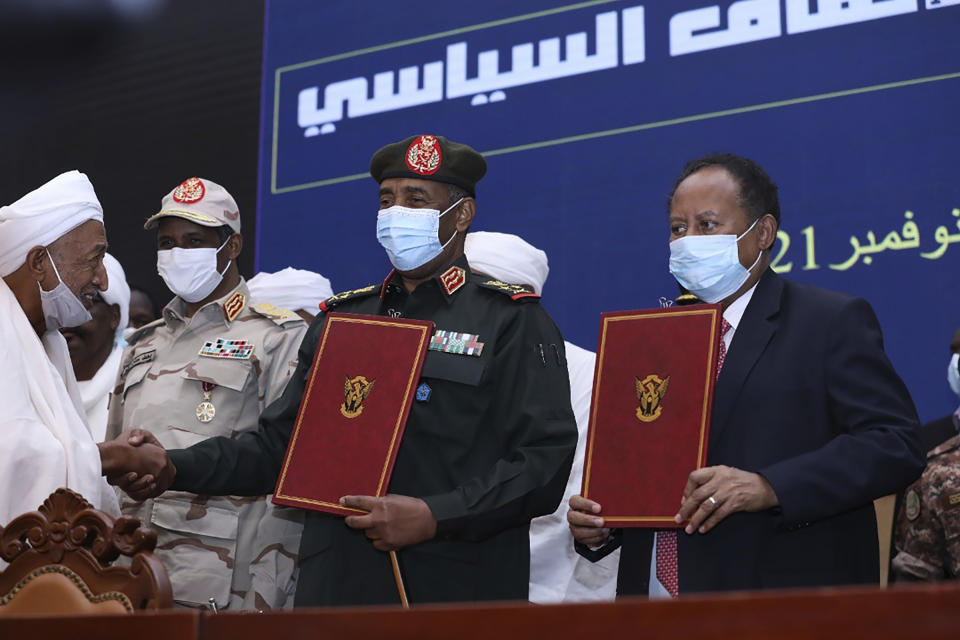 FILE - In this photo provided by the Sudan Transitional Sovereign Council, Sudan's top general Abdel Fattah Al-Burhan, center, and Prime Minister Abdalla Hamdok hold documents attended by Gen. Mohammed Hamdan Dagalo, second left, during a ceremony to reinstate Hamdok, who was deposed in a coup last month, in Khartoum, Sudan, Nov. 21, 2021. A year after a military takeover upended Sudan’s transition to democracy on Oct. 25, 2021, growing divisions between the two powerful branches of the armed forces are further endangering Sudan’s future. (Sudan Transitional Sovereign Council via AP, File)