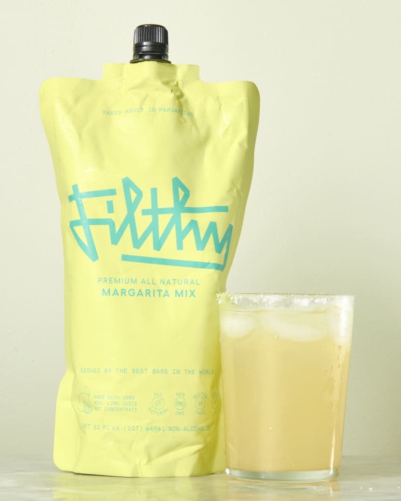 photo of Filthy Margarita mix pouch with a mixed drink next to it on a marble surface with a light green background