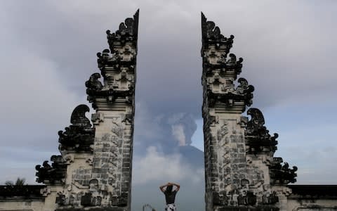 A tourist watches as Mount Agung volcano erupts at Lempuyang Temple in Karangasem, Bali  - Credit: Reuters