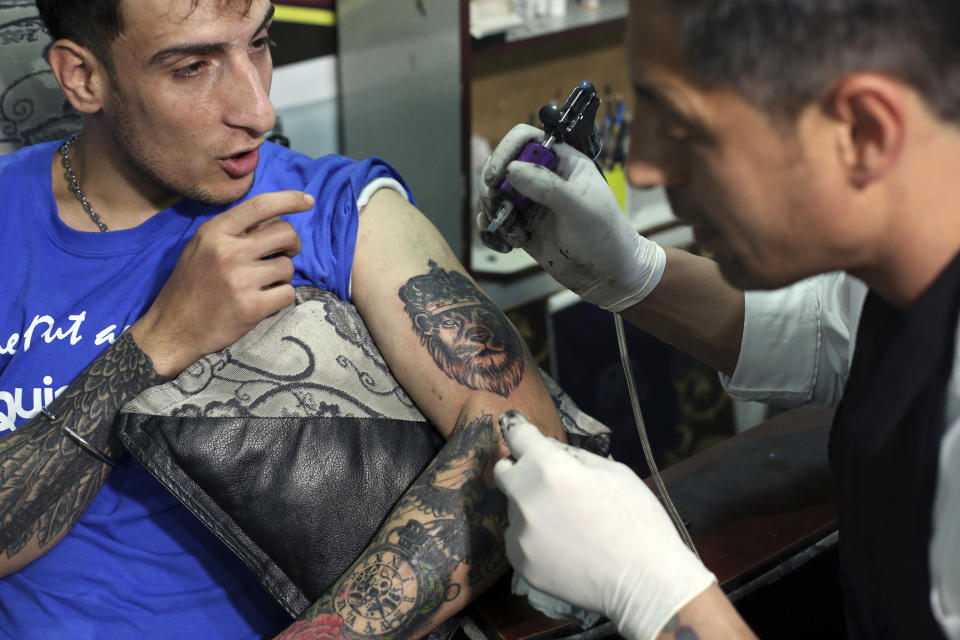 In this Wednesday, Nov. 20, 2019, photo, Omid Noori, 23, left, gets a lion tattoo on his left arm by Nazeer Mosawi, a tattoo artist in Kabul, Afghanistan. Mosawi, 42, fought for seven years in Afghanistan’s civil war with the Islamic insurgents. He says he is still fighting the war, but this time his battle is against society’s conservatism, with his tattoo machine as his weapon. (AP Photo/Rahmat Gul)