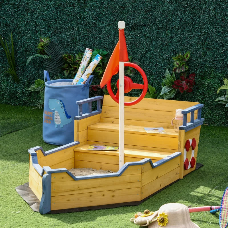 Children's wooden sandbox with a boat theme, complete with a steering wheel and flag, and a storage bag attached