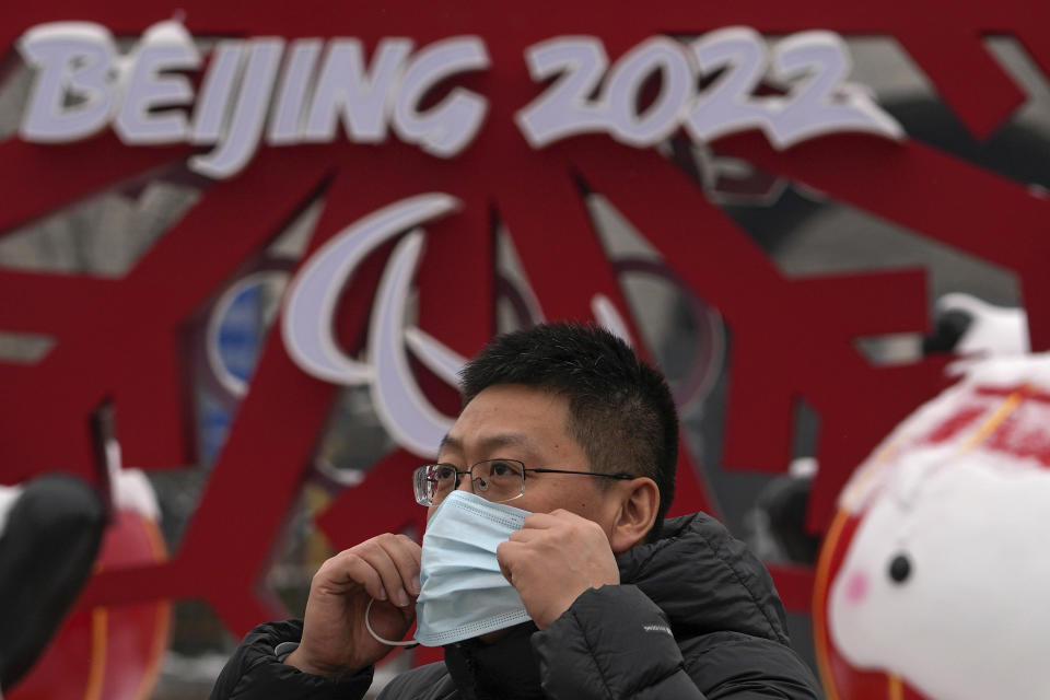 A man puts on his face mask to help protect from the coronavirus as he walks by a decoration for the Beijing Winter Olympics Games at Qianmen Street, a popular tourist spot in Beijing, Sunday, Jan. 23, 2022. Chinese authorities have called on the public to stay where they are during the Lunar New Year instead of traveling to their hometowns for the year's most important family holiday. (AP Photo/Andy Wong)